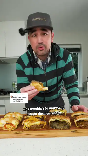 A man in a cap in his kitchen holding up a pie