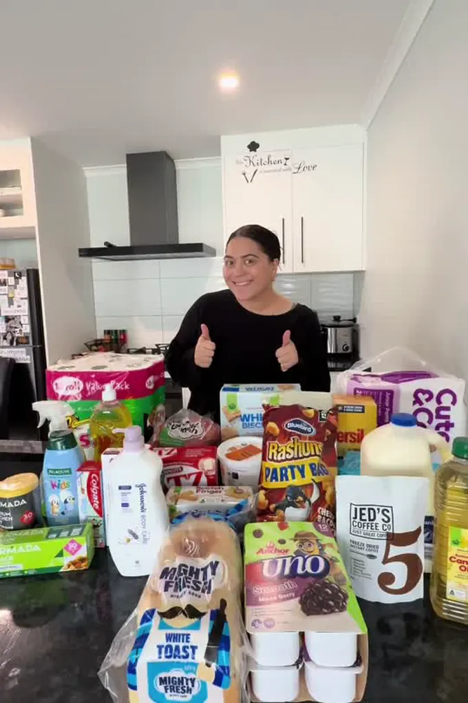 Example post, a photo: a woman giving two thumbs up behind a kitchen bench piled with her weekly grocery shop