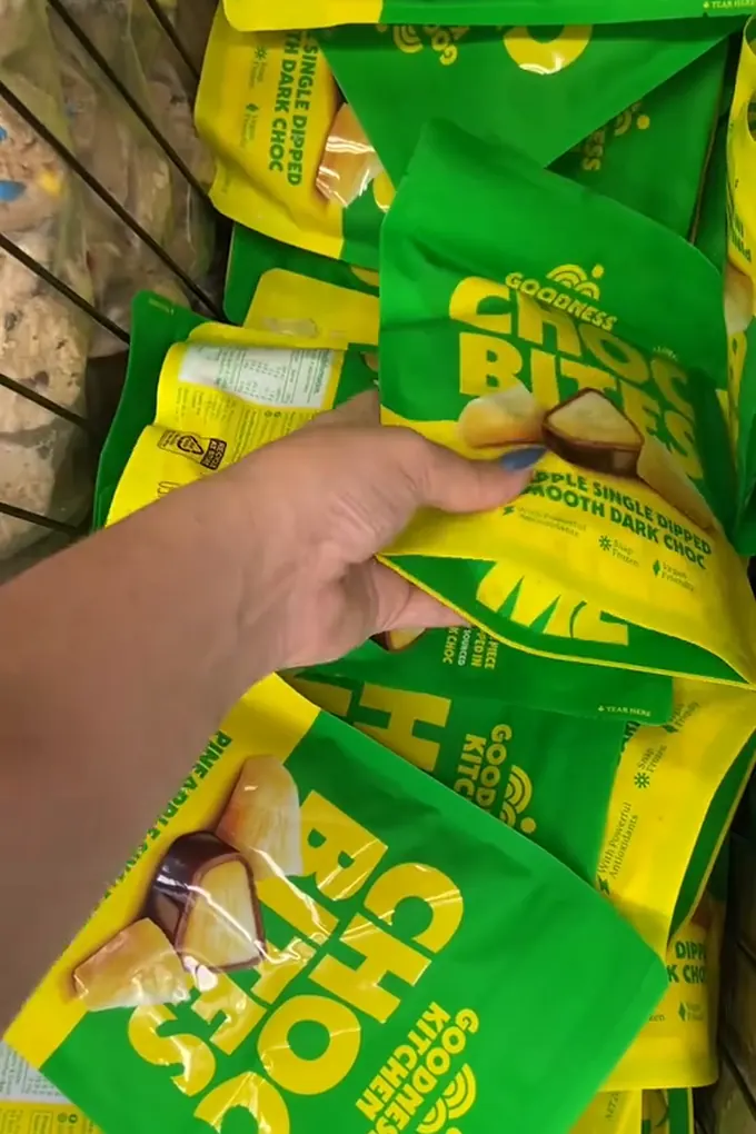 Example post, a photo: a hand picking a pouch of chocolate-coated snacks off a supermarket shelf